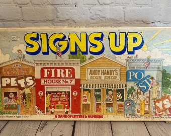May include: A vintage board game box for "Signs Up", a game of letters and numbers. The box features colourful illustrations of various shops with signs, including a fire station, a pet shop, a sign shop, and a post office. The game is for 2 to 4 players, ages 6 to 10.