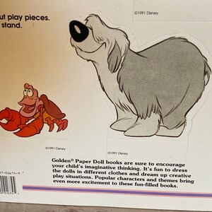 May include: A vintage Golden Paper Doll book featuring a red crab and a grey dog. The book cover includes the text "Golden Paper Doll books are sure to encourage your child's imaginative thinking. It's fun to dress the dolls in different clothes and dream up creative play situations. Popular characters and themes bring even more excitement to these fun-filled books."