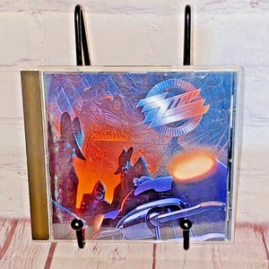 Puede incluir: Una caja de CD con una imagen colorida de una banda en la parte delantera. El nombre de la banda es "ZZ Top" y el título del álbum es "Afterburner".