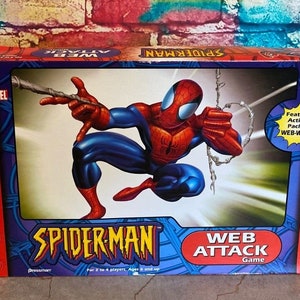May include: A Spider-Man Web Attack game box featuring a dynamic illustration of Spider-Man in his red and blue suit, shooting a web. The box is red and blue with the Marvel logo and game title.