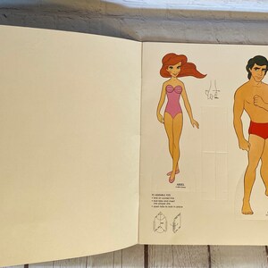 May include: A paper doll set featuring Ariel and Eric from the Disney movie The Little Mermaid. The dolls are printed on cardstock and are ready to be cut out and assembled. Instructions for assembling the dolls are included on the page.