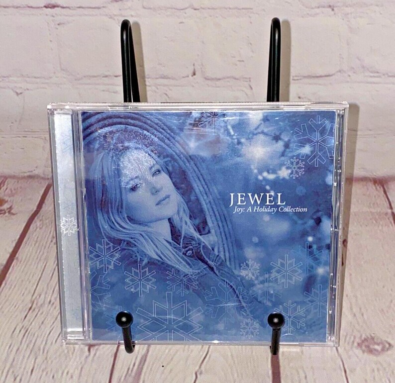May include: Jewel's "Joy: A Holiday Collection" CD features a blue and white wintery design with a snowflake pattern and a photo of Jewel on the front.
