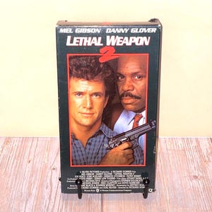 May include: A VHS tape for the movie "Lethal Weapon 2" featuring Mel Gibson and Danny Glover. The cover has a dark green border with the movie title in red and the actors' faces.