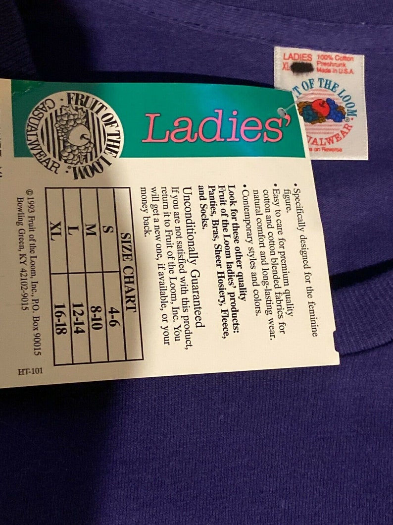 May include: A purple Fruit of the Loom t-shirt with a white tag that says "Ladies'" and has a size chart. The tag also says "Unconditionally Guaranteed" and includes information about the brand and its products.