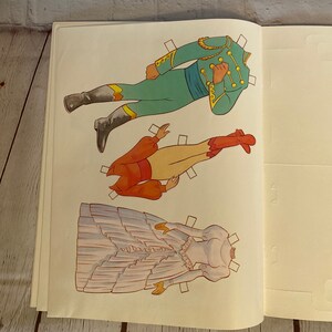 May include: A vintage paper doll set featuring a couple in traditional attire. The woman wears a white gown with a ruffled skirt and a red bodice. The man wears a green jacket with gold trim and red trousers. The paper dolls are ready to be cut out and played with.