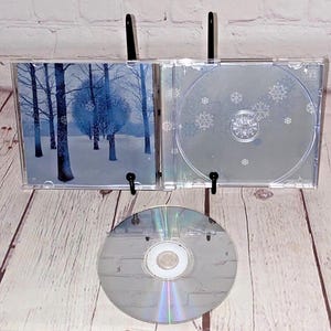May include: A clear plastic CD case with a wintery forest scene on the front and a snowflake design on the back. The CD is included and is silver.