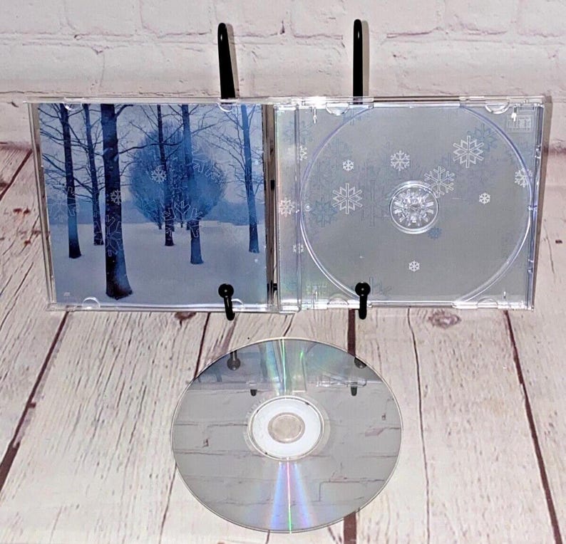 May include: A clear plastic CD case with a wintery forest scene on the front and a snowflake design on the back. The CD is included and is silver.