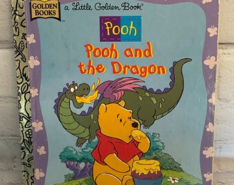 Puede incluir: Un libro pequeño dorado de color morado y azul con un logotipo de sol amarillo. El libro presenta a Winnie the Pooh y un dragón verde. El título es "Pooh and the Dragon".