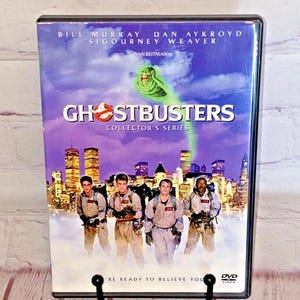 May include: DVD case for the movie Ghostbusters, featuring the main cast members Bill Murray, Dan Aykroyd, and Sigourney Weaver. The case is purple and features a cityscape with the Ghostbusters logo and the text "Collector's Series".