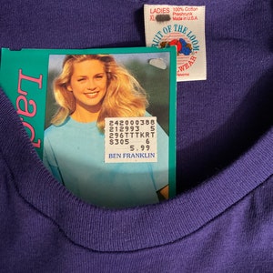 May include: A purple Fruit of the Loom t-shirt with a white tag that says "LADIES 100% Cotton Preshrunk Made in U.S.A XL" and a price tag that says "242000388 212993 5 296TTTKRT $305 6 5.99 BEN FRANKLIN".