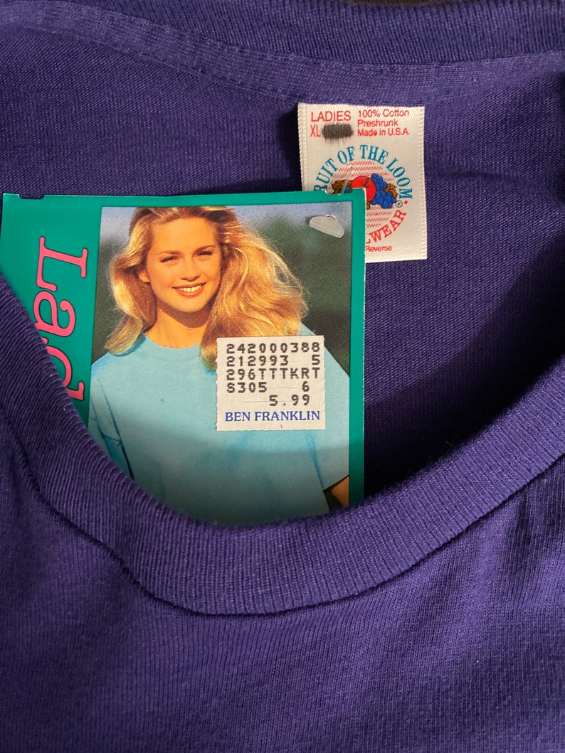 May include: A purple Fruit of the Loom t-shirt with a white tag that says "LADIES 100% Cotton Preshrunk Made in U.S.A XL" and a price tag that says "242000388 212993 5 296TTTKRT $305 6 5.99 BEN FRANKLIN".