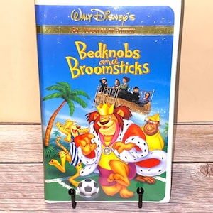 May include: A VHS tape of Walt Disney's "Bedknobs and Broomsticks" 30th Anniversary Edition. The cover features a vibrant illustration of a lion in a crown, a cheetah, and a soccer ball against a blue sky background. The title is in yellow and orange.