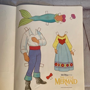 May include: A paper doll set featuring Ariel, Prince Eric, and a mermaid tail from the Disney film The Little Mermaid. The paper dolls are ready to be cut out and played with.