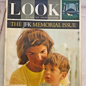 May include: A magazine cover featuring a black and white photo of a casket with the word "LOOK" in large white letters. The magazine cover also features a color photo of Jacqueline Kennedy Onassis and her son John Jr. The text on the cover reads "NOW MORE THAN 7,500,000 CIRCULATION" and "THE JFK MEMORIAL ISSUE".