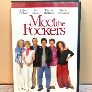 May include: A DVD case for the movie Meet the Fockers featuring the names Robert De Niro, Ben Stiller, Dustin Hoffman, and Barbra Streisand at the top. The cover displays a group of six people standing in a line against a white background.