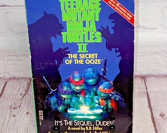Puede incluir: Un libro de bolsillo titulado "Teenage Mutant Ninja Turtles II: The Secret of the Ooze". La portada presenta a las cuatro tortugas con sus máscaras de colores, y el texto "It's the Sequel, Dudes!" también es visible.