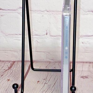 May include: A black metal CD stand with a Jewel - This Way album in a clear plastic case. The stand has two rounded ends and a rectangular base.