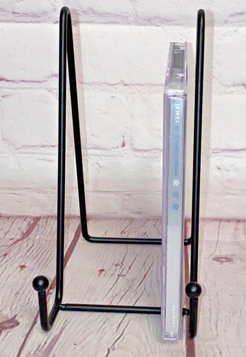 May include: A black metal CD stand with a Jewel - This Way album in a clear plastic case. The stand has two rounded ends and a rectangular base.
