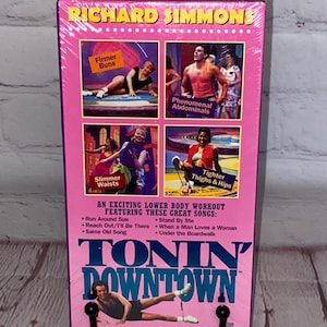 May include: A pink and white VHS tape case with a photo of Richard Simmons on the front. The case is titled "Tonin' Downtown" and features a lower body workout with songs like "Run Around Sue" and "Stand By Me".