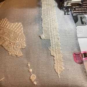 Puede incluir: Primer plano de un proyecto de costura en curso. Una tela azul claro est&aacute; adornada con encaje beige y costuras decorativas. Se ve una aguja de m&aacute;quina de coser, junto con una pinza rosa.