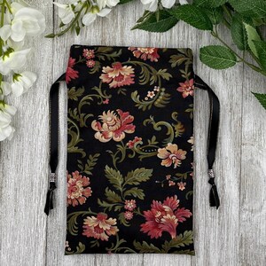 May include: A black drawstring bag with a floral pattern in shades of pink, cream, and green. The bag has black satin drawstrings with silver beads at the ends.