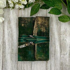 May include: A green and gold fabric journal with a crystal charm and gold ribbon tied around it.