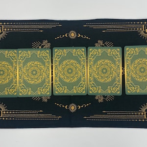 Puede incluir: Un pa&ntilde;o de tarot negro con dise&ntilde;os celestiales dorados y un borde. Seis cartas de tarot verdes con detalles dorados est&aacute;n dispuestas sobre el pa&ntilde;o. Las cartas tienen un dise&ntilde;o circular en el centro.