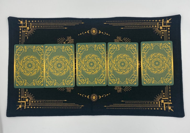 Puede incluir: Un pa&ntilde;o de tarot negro con dise&ntilde;os celestiales dorados y un borde. Seis cartas de tarot verdes con detalles dorados est&aacute;n dispuestas sobre el pa&ntilde;o. Las cartas tienen un dise&ntilde;o circular en el centro.