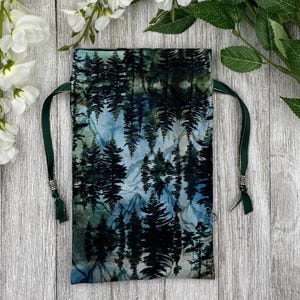 May include: A green drawstring bag with a forest scene print. The bag is made of fabric and has a dark green drawstring.
