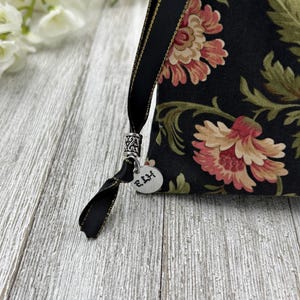 May include: A black fabric pouch with a floral pattern and gold trim. The pouch has a black ribbon with a silver charm that says "E.H.H."