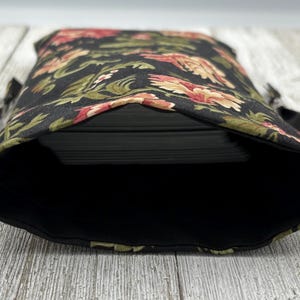 May include: Black fabric bag with a floral print in shades of red, green, and white. The bag is open and empty, showing the black lining.