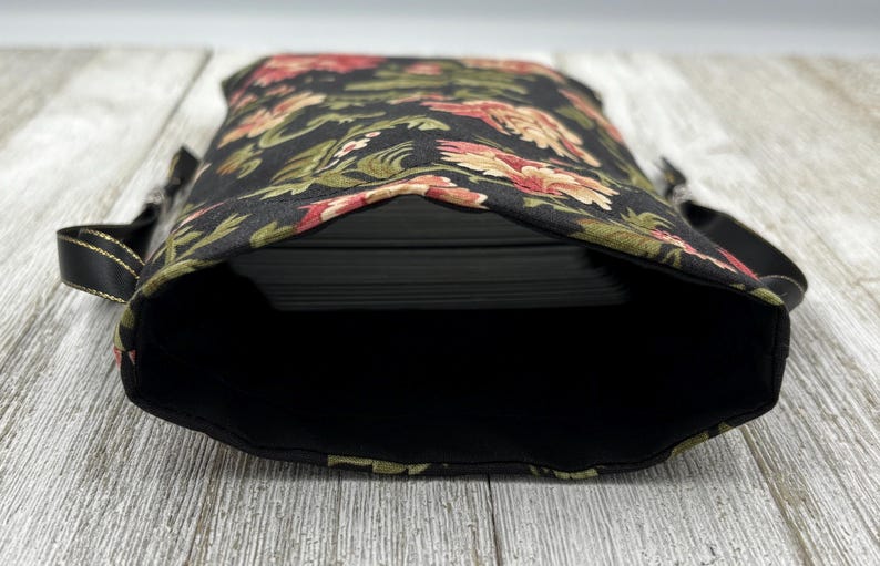 May include: Black fabric bag with a floral print in shades of red, green, and white. The bag is open and empty, showing the black lining.