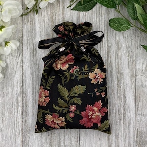May include: A black drawstring bag with a floral pattern and a black ribbon with gold trim. The bag has silver beads on the drawstring.