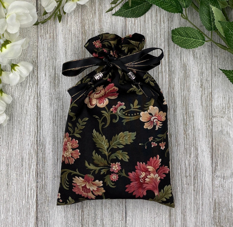 May include: A black drawstring bag with a floral pattern and a black ribbon with gold trim. The bag has silver beads on the drawstring.