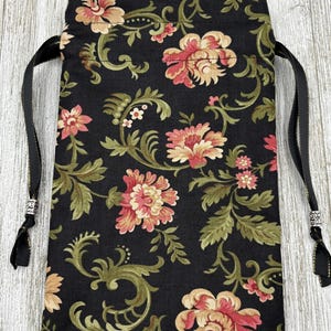 May include: A black drawstring bag with a floral pattern. The bag has a black and gold drawstring with silver beads on the ends.