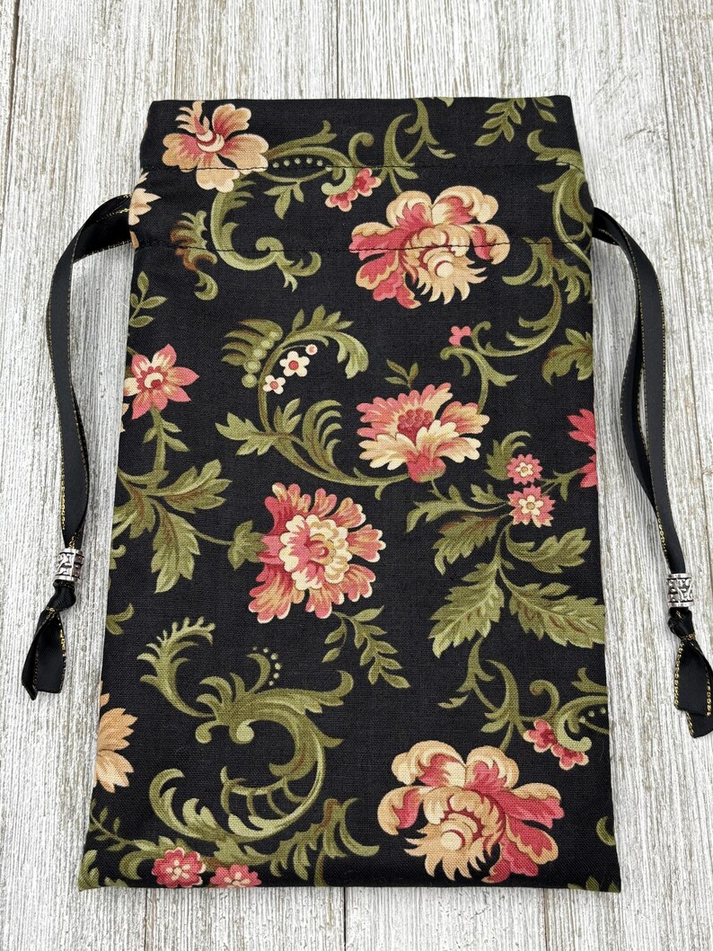 May include: A black drawstring bag with a floral pattern. The bag has a black and gold drawstring with silver beads on the ends.