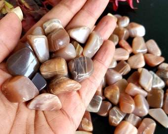 May include: A collection of polished moonstones in various shades of brown, tan, and gray. The stones are smooth and rounded, with a subtle sheen. The image is a close-up, showcasing the natural beauty and variations in color and texture of the stones.