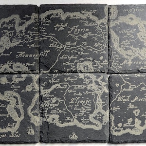 May include: A set of six square black slate coasters arranged in a grid, each featuring a detailed laser-engraved map of the continent of Tamriel. The map includes labels for regions like Skyrim, Morrowind, and Black Marsh, with a compass rose.