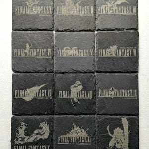 Op de afbeelding: Een set van twaalf vierkante onderzetters van zwarte leisteen, elk gegraveerd met een uniek Final Fantasy-logo en Romeinse cijfers van I tot XII. De donkere steentextuur vormt een contrast met de lichtgekleurde gegraveerde afbeeldingen.