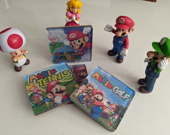 Może przedstawiać: Kolekcja przedmiotów z motywem Super Mario Bros. Zawiera figurki Mario, Luigiego, Toada i Księżniczki Peach, a także podkładki pod napoje z motywem gier Mario Tennis, Mario Golf i Super Mario 64.