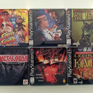May include: Six PlayStation game cases, all with different titles. The cases are black with a blue PlayStation logo. The games are: Street Fighter Collection, Street Fighter Alpha 2, Legacy of Kain: Soul Reader, Metal Gear Solid, Bloody Roar, and Blood Omen: Legacy of Kain.