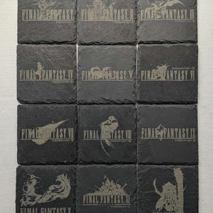 Peut inclure: Un ensemble de douze dessous de verre carrés en ardoise. Chaque dessous de verre présente un titre et une illustration différents de Final Fantasy, gravés en couleur claire sur l'ardoise gris foncé. Les dessous de verre sont disposés en grille.