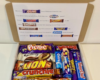 May include: A brown cardboard box filled with a variety of chocolate bars. The box is open and the chocolate bars are visible. The chocolate bars include brands such as Picnic, Galaxy, Wispa, Twirl, Crunchie, Lion, and Smarties.