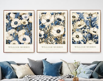 May include: Three framed prints of botanical illustrations featuring white and blue flowers with gold accents. The prints are titled "William Morris" and are arranged in a row on a white wall.