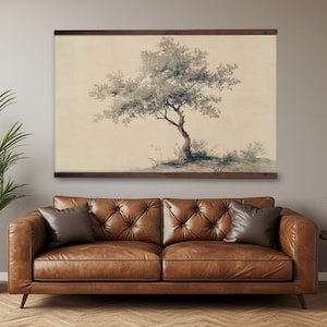 May include: A framed print of a tree with a light beige background. The tree is depicted in shades of gray and brown, with a detailed trunk and branches. The frame is a dark brown color. The print is hanging above a brown leather sofa.