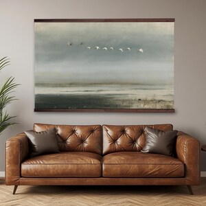 Peut inclure: Une tenture murale rectangulaire présentant une impression paysagère d'un vol d'oiseaux blancs au-dessus d'un marais brumeux aux tons sourds. L'œuvre est fixée entre deux baguettes en bois brun foncé en haut et en bas, créant un aspect de rouleau.