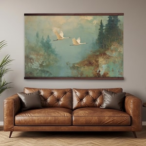 Könnte beinhalten: Ein rechteckiger Wandbehang mit einem Landschaftsgemälde von zwei weißen Kranichen im Flug über einem nebligen Wald in gedeckten Grün-, Braun- und Blautönen. Das Kunstwerk ist zwischen zwei horizontalen dunklen Holzleisten oben und unten befestigt.