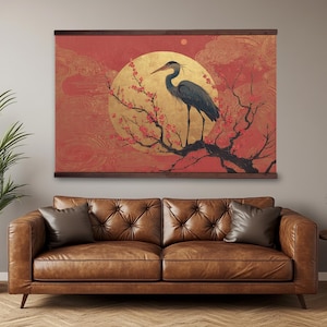 Pode incluir: Uma tapeçaria de parede com design de inspiração asiática. Apresenta uma garça azul pousada num galho florido, contra um sol dourado e um céu vermelho. A obra é emoldurada em madeira escura, ideal para uma sala de estar.