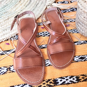 Peut inclure: Une paire de sandales en cuir marron avec des lanières croisées. Les sandales ont un design simple et sont faites de cuir de haute qualité.