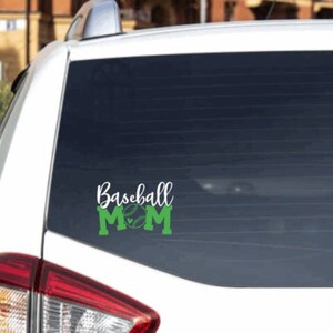 May include: White car with a green and white vinyl decal on the rear window that says "Baseball Mom" with a baseball and heart graphic.